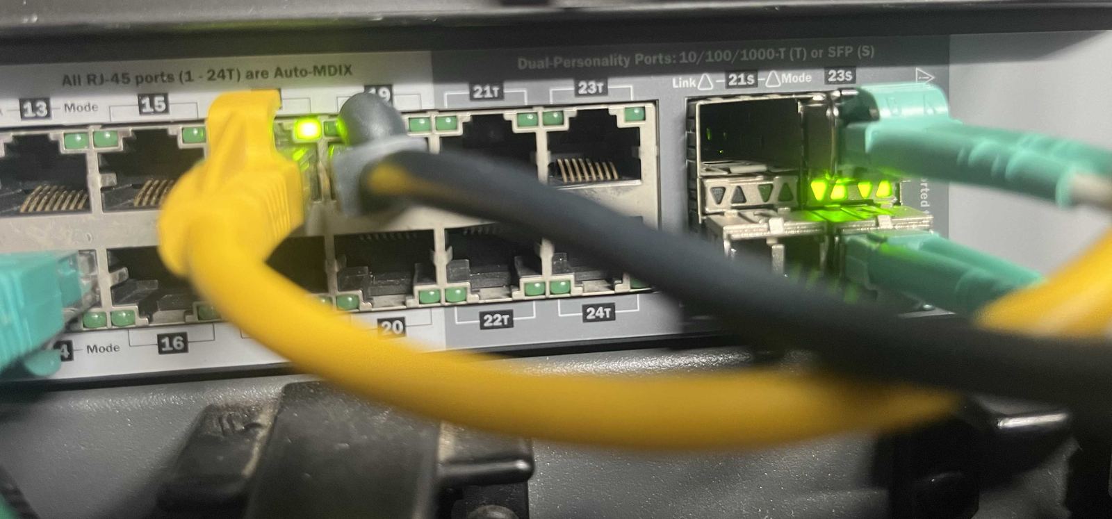 Yellow and black ethernet cables alongside aqua OM3 fibre uplinks on a network switch.
