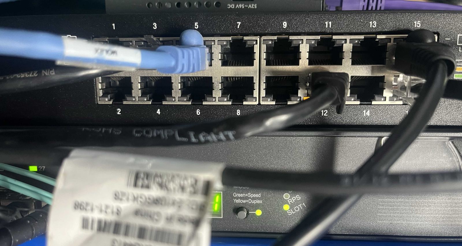 A patch panel and switch with a mix of blue, black, purple and teal ethernet and fibre cables.